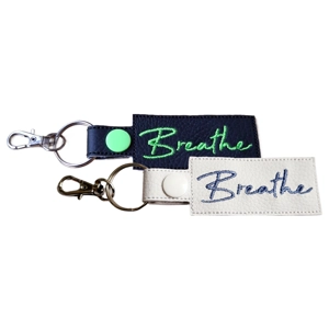 Two faux leather keyrings embroidered with the word ‘Breathe’, shown in black and white colour options with metal keyring hardware.