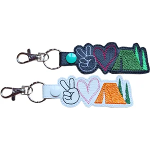 Black and white Camping Peace Love faux leather keyrings with embroidered peace sign, heart, tent and trees design.