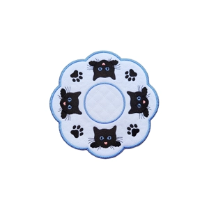 Round embroidered decorative mat with scalloped edges, featuring four black cat faces with blue eyes and pink noses, along with black pawprints on a white background with an embroidered stippled pattern.