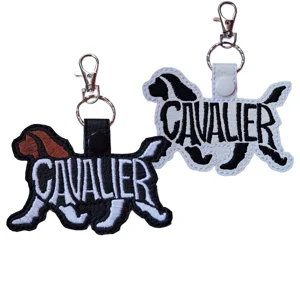 Black and white Cavalier word art keyrings with embroidered details, shown with metal keyrings and clasps.