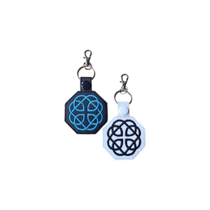 Two Celtic Fatherhood Knot keyrings made from faux leather. One keyring is black with bright blue embroidered knotwork and a black snap fastener; the other is white with black embroidered knotwork and a white snap fastener. Both have an octagonal shape and are attached to metal rings with swivel lobster clasps.