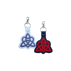 Two Celtic Trinity Heart keyrings displayed on a white background, one in white faux leather with grey embroidery and one in black faux leather with red embroidery, each finished with a metal keyring and lobster clasp.