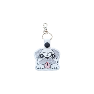 A kawaii-style pug dog keyring made from faux leather, featuring an embroidered pug face with big eyes, floppy ears, and a small tongue-out smile, finished with a metal keyring and lobster clasp.