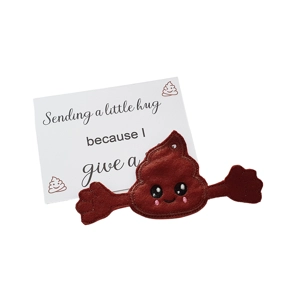 A brown felt poop character with a cute smiling face, rosy cheeks, and outstretched arms, attached to a keyring. Behind it is a white keepsake card that reads “Sending a little hug because I give a…” with small cartoon poop icons in the corners.