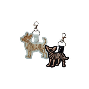 Two embroidered Chihuahua-shaped keyrings made from faux leather. One is white with tan stitching, and the other is black with tan stitching. Both feature the word 'Chihuahua' stitched across the body and have metal keyrings with clasps attached at the top.