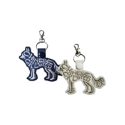 Two Chinese Crested dog-shaped keyrings made from faux leather, one in black and one in white. Both feature embroidered outlines and stitched word-art spelling Chinese Crested, with a metal ring and swivel clasp attached at the top.