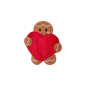A felt gingerbread character holding an oversized heart-shaped chocolate box with a stitched ribbon, featuring embroidered facial details.