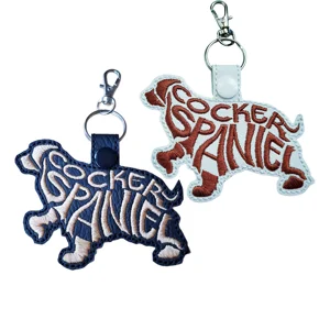 Two Cocker Spaniel word art keyrings in black and white faux leather, embroidered with breed lettering and finished with metal keyring clips.
