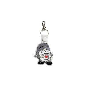 White faux leather keyring featuring an embroidered gnome with a grey hat, fluffy white beard, and beige nose, holding a white mug with a red heart. Finished with a white snap and silver keyring clasp.
