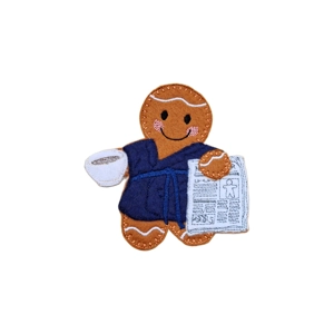 A felt gingerbread character wearing a robe, holding a cup of coffee in one hand and a newspaper in the other.