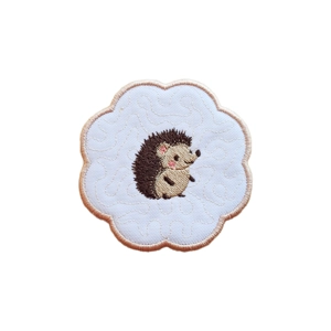 A scalloped candle coaster featuring a sweet embroidered hedgehog on white fabric with a subtle stitched background and a neatly finished stitched border.