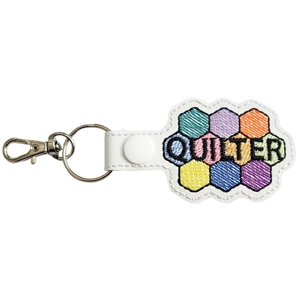 Quilter keyring made of white faux leather featuring colourful embroidered hexagon patches forming the word Quilter, attached to a white snap strap with a metal keyring and lobster clasp.