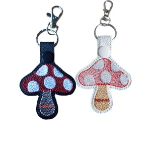 Two embroidered toadstool keyrings shown in black and white faux leather options, each with red and white mushroom stitching and silver keyring hardware.