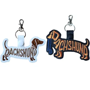 Two Dachshund word art keyrings in black and white faux leather, embroidered with breed lettering and finished with metal keyring clips.