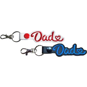 Two Dad keyrings with embroidered lettering and heart detail, shown in black and white faux leather with metal lobster clasps.