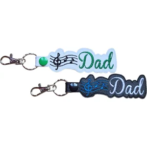 Two Dad music keyrings shown in black and white faux leather with embroidered musical notes, Dad lettering and metal lobster clasps.