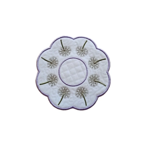 Dandelion Clock Decorative Table Mat featuring delicate embroidered dandelion clocks in a circular design, with a subtle stippling pattern and a scalloped edge finished with a light lavender border.