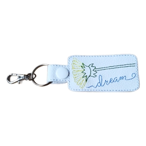 White faux leather keyring embroidered with a dandelion stem and the word dream in green and blue thread. Finished with a white snap, metal ring, and lobster clasp.