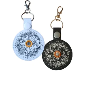 Black and white faux leather dandelion seed head keyrings with embroidered floral seed designs and metal clip hardware.
