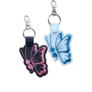Black and white Flowing Wing Butterfly keyrings with pink and teal embroidery, faux leather straps and metal lobster clasps.