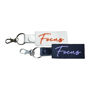 Two faux leather affirmation keyrings embroidered with the word “Focus”, shown in black and white colour options with metal keyring and lobster clasp attachments.