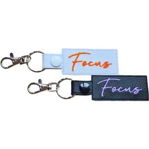Black and white faux leather Focus positive word keyrings with embroidered text and metal clip attachments.