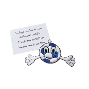 A football-themed felt pocket hug keyring featuring a smiling blue and white football with green embroidered eyes and outstretched white arms ending in mitten-shaped hands. It is paired with a white keepsake card that reads: ‘Sending a hug from me to you, Just because I wanted to, A hug to show you that I care, From over here, to over there’.