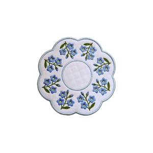 Forget Me Not Decorative Table Mat with scalloped edges, delicate blue embroidered flowers, green leaves, and a subtle stippling pattern on a white waterproof fabric.