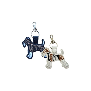 Two fox terrier–shaped faux leather keyrings with embroidered word art. One is black with tan and light blue stitching and a silver clasp, and the other is white with brown and black stitching and a gold clasp. Both feature a snap tab and attached keyring.