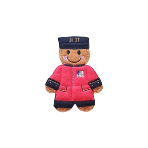 Gingerbread Chelsea Pensioner Character – a handmade felt gingerbread figure dressed as a Chelsea Pensioner, wearing a red uniform with black cuffs and hat embroidered with the initials “RH,” decorated with small stitched medals and a smiling face.