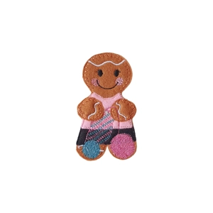 A handmade felt gingerbread character dressed in a pink top and dark skirt, holding a crochet project with two colourful yarn balls — one teal and one pink.
