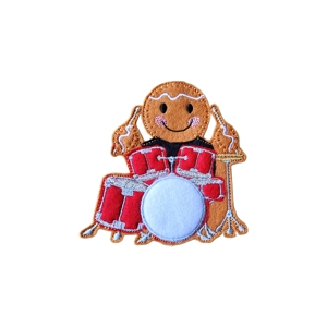 A felt gingerbread drummer character holding drumsticks, sitting behind a red and white embroidered drum kit with golden cymbal details. The gingerbread has pink cheeks, a smiling face, and white icing trim, crafted from soft felt with detailed stitching.