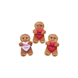 Three handmade felt gingerbread characters holding heart-shaped felt hearts with embroidered icing-style details and smiling faces. Each heart features a stitched message, such as “Miss You,” “Hugs,” or a personalised text option.