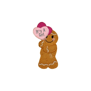 Handmade felt gingerbread character holding two pink heart-shaped balloons, one embroidered with the words ‘It’s a Girl’, decorated with stitched icing details and a cheerful smile.