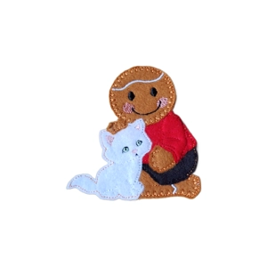 Handmade felt gingerbread character sitting beside a small felt cat. The gingerbread has stitched icing-style details, rosy cheeks, and a cheerful smile. A sweet handcrafted decoration symbolising friendship and love.