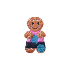 A felt gingerbread character with embroidered details, a smiling face, and rosy cheeks, wearing a pink top and a black skirt, working on their latest knitting project.