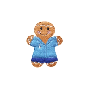 Handmade felt gingerbread nurse character wearing blue scrubs, smiling with embroidered details and icing-style accents on the arms and legs.