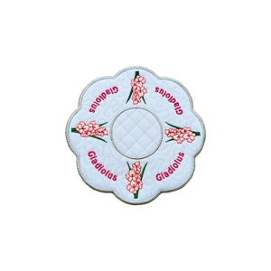Embroidered round scalloped table mat with pink Gladiolus flowers and the word ‘Gladiolus’ stitched around the edges, featuring a stippled pattern and bold borders