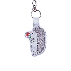 Embroidered faux leather hedgehog keyring holding a red flower, attached to a metal clasp and ring.