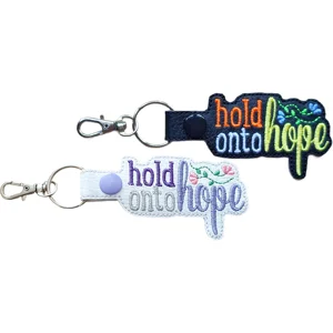 Two Hold Onto Hope keyrings in black and white faux leather, with colourful embroidered positive wording, floral details and silver metal hardware.