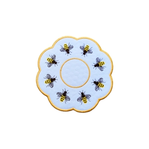 Round embroidered decorative table mat with a scalloped edge, featuring yellow and black honey bee designs atop a stippled pattern on a white background with gold borders.