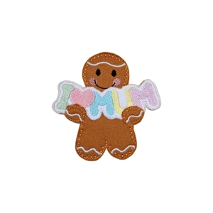 A felt gingerbread character holding an embroidered ‘I ♥ MUM’ banner in soft pastel colours, with stitched icing details, a smiling face, and rosy cheeks.