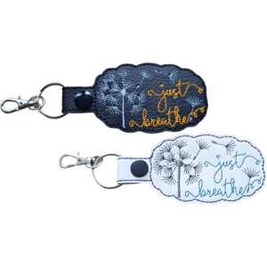 Black and white faux leather Just Breathe dandelion mindfulness keyrings with embroidered dandelion designs and metal clip hardware.