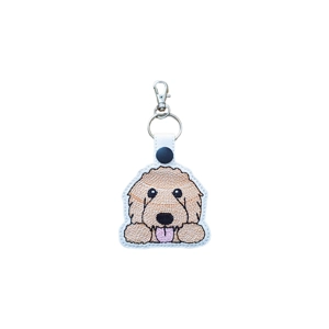 Kawaii-style embroidered Goldendoodle keyring featuring a fluffy doodle face with curly fur, bright eyes and a tongue-out smile, attached to a white faux leather strap with a metal ring and lobster clasp.