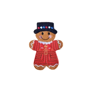 A felt gingerbread beefeater character wearing a red uniform with gold embroidered details and a black hat, smiling and standing upright.