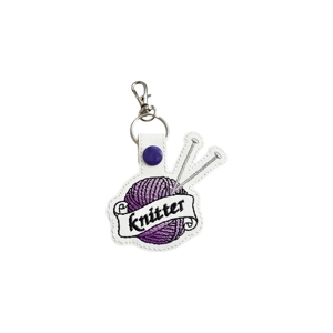 A faux leather knitter keyring featuring a purple stitched ball of yarn with two grey knitting needles and the word ‘Knitter’ embroidered across the front, finished with a silver keyring and lobster clasp.
