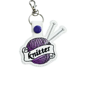 White faux leather Knitter keyring with purple wool ball, silver knitting needles embroidery and metal keyring clip.