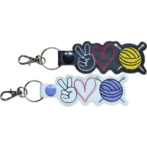 Black and white Knitting Peace Love keyrings featuring embroidered peace signs, hearts and yarn balls with knitting needles, finished with metal keyring hardware.