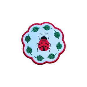 Ladybird candle coaster with a red embroidered ladybird, green leaves, red scalloped border, and softly stitched white background.