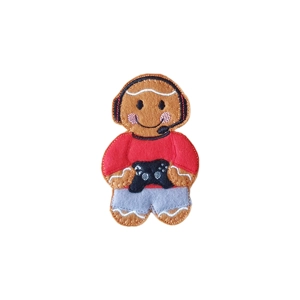 A gingerbread gamer character wearing a gaming headset and holding a controller, dressed in a long-sleeved top and trousers, with a friendly smiling expression.
